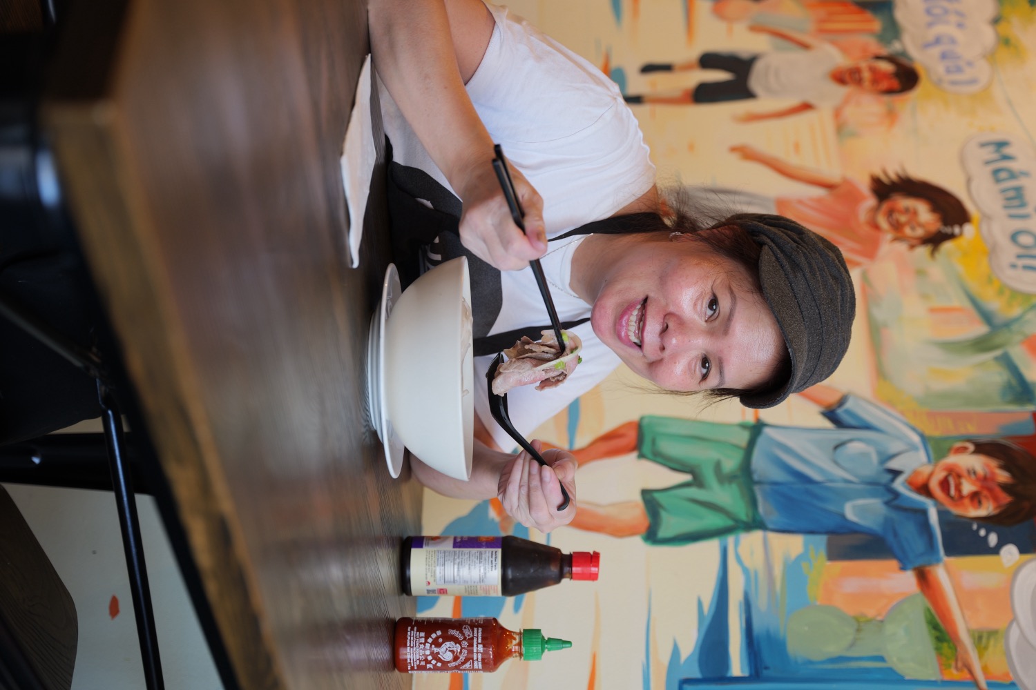Mámì with a fresh bowl of pho in front of the Chào Mámì mural